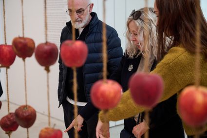 Three visitors stand behind a curtain of threaded apples.
