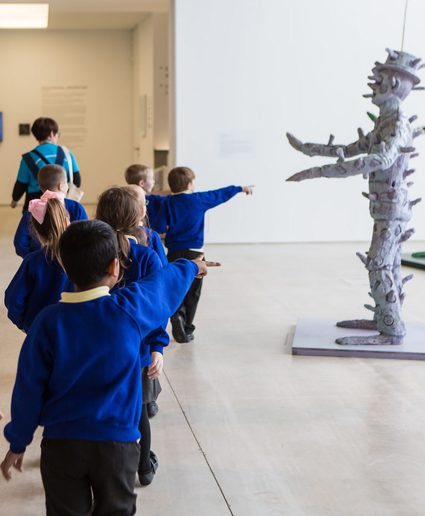 A group of schoolchildren look at a tall, white, sculptural figure in the Sunley Gallery at Turner.